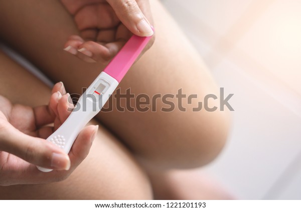 Unhappy young asian woman\
holding pregnancy test showing a negative result in her bathroom,\
wellness and healthy concept, infertility problem,Selective\
focus.