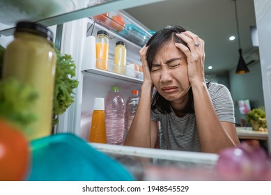 unhappy young asian woman looking inside the fridge