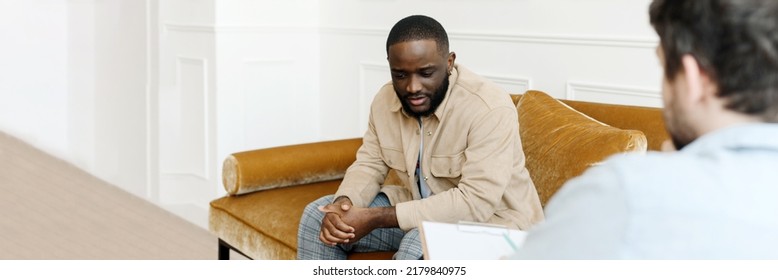 Unhappy Young Black Man Gay Having Session With Professional Psychologist At Mental Health Clinic. Professional Psychological Help Concept. Web Banner