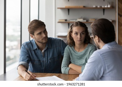 Unhappy young Caucasian couple buyers talk with male realtor or real estate agent dissatisfied with contract terms regulations. Upset angry clients frustrated with deal on consultation with broker.