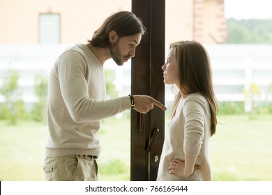 Unhappy young couple arguing standing at house door, angry husband pointing at wife blaming her of problems, conflicts in marriage, bad relationships, man and woman having quarrel or disagreement