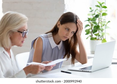 Unhappy young female employee bored with middle-aged colleague discuss paper document at meeting. Tired woman worker bothered annoyed by senior coworker lecture about paperwork at team briefing. - Shutterstock ID 2000992940