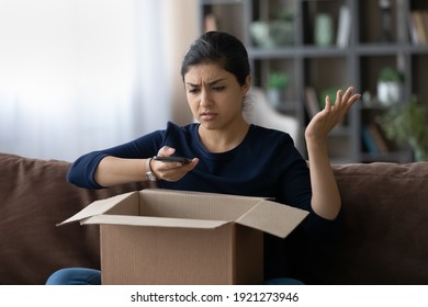 Unhappy young Indian woman frustrated by wrong order shopping online using smartphone. Upset ethnic female buyer unbox parcel buying on web confused with bad delivery service. Shipping concept.