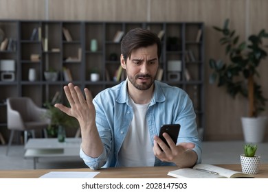 Unhappy Young Man Looking At Phone, Feeling Nervous Of Bad Device Work, Internet Disconnection, Lost Data Or Inappropriate Online Content. Anxious Male User Dissatisfied With Application Or Service.