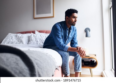 Unhappy Young Man With Mental Health Issues Sitting On Edge Of Bed