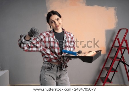 Unhappy young woman with bad expression near wall at home, showing thumb down gesture. Renovation, repair and redecoration concept. [[stock_photo]] © 