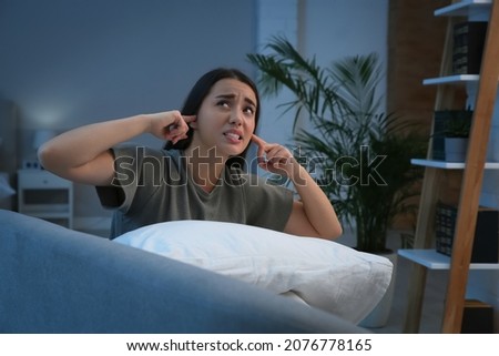 Unhappy young woman covering ears in living room at night. Noisy neighbours