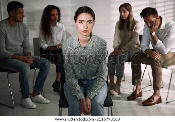 Unhappy young woman and group of people behind\
her back indoors. Therapy\
session
