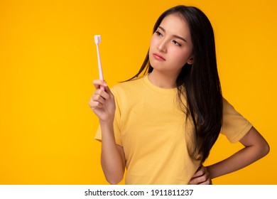 Unhappy young woman look at toothbrush, get unsatisfied it Attractive beautiful girl can’t choose good quality of toothbrush Pretty lady get confused and curious Dental care concept Yellow background