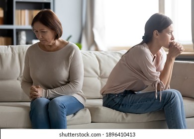 Unhappy young woman and mature mother avoiding talking after quarrel, elderly mum and grownup daughter sitting on couch back to back separately, two generations of women conflict concept