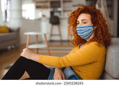 Unhappy young woman with red curly hair with face protective mask leaned on sofa in living room during COVID-19. - Powered by Shutterstock