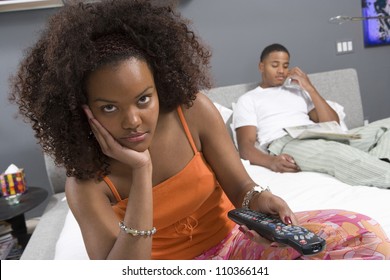 Unhappy young woman watching TV while a man makes a call