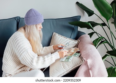 Unhappy Young Woman Wearing Warm Clothing At Home And Counting Cash Money. Energy Crisis In Europe Due To Inflation And War. Increase In The Price Of Natural Gas For Home Heating. 