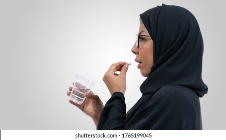 Unhealthy Arabic Woman With Pained Facial Expression Feels Unwell, Suffering From Migraine Headache, Takes Pill Analgesic Medication To Relieve Pain, Stressed Lady Holds Tablet And Glass Of Water.