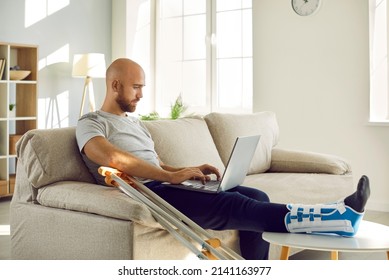 Unhealthy businessman with injured leg in bandage sit on sofa at home work online on computer. Unwell male employee with foot trauma wearing special splint use laptop. Injury and rehabilitation. - Shutterstock ID 2141163977