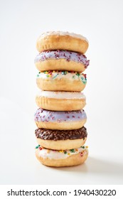 Unhealthy Desserts. Impressive Tower Of Various Sweet Colorful Donuts With Sprinkles And Glaze Isolated Over Light Background. Unhealthy Eating And Junk Food Concept