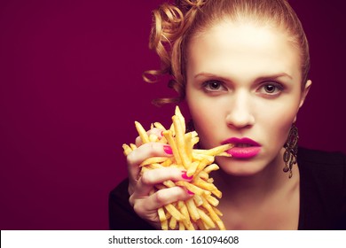 Unhealthy eating. Junk food concept. Portrait of fashionable young woman holding (eating) fried potato (fries, chips) in her hand and posing over purple background. Close up. Copy-space. Studio shot