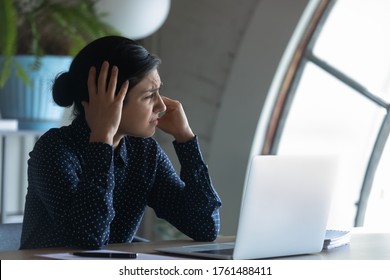 Unhealthy Fatigued Indian Overworked Employee Sitting At Workplace Looks At Window Frown Suffering From Strong Headache, Loud Noises Or Hangover, Having High Blood Pressure, Feeling Stressed At Work