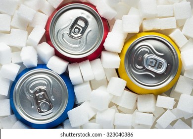 Unhealthy Food Concept - Sugar In Carbonated Drinks. Sugar Cubes As Background And Canned Drinks 