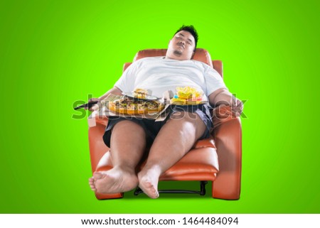 Unhealthy lifestyle concept: Young obese man sleeping with junk foods on the armchair with green screen background