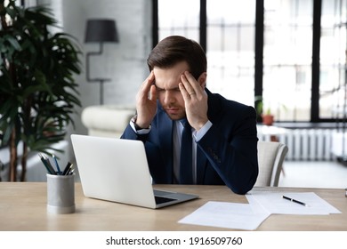 Unhealthy Male Employee Sit At Desk In Office Struggle From Dizziness Overwork On Computer. Unwell Tired Caucasian Businessman Work On Laptop Suffer From Headache Or Migraine. Health Problem Concept.