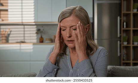 Unhealthy mature elderly upset tired Caucasian woman grandmother suffering from headache holding head temples feeling pain fatigued suffer from migraine symptom panic attack pressure at home on couch - Powered by Shutterstock