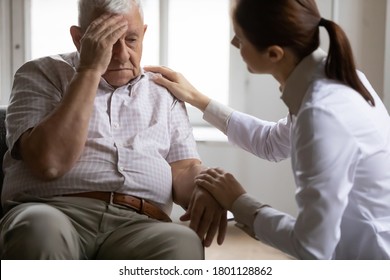 Unhealthy mature old patient complaining to doctor about head ache migraine illness at checkup meeting in clinic. Professional young female general practitioner giving advice, treating elderly man.