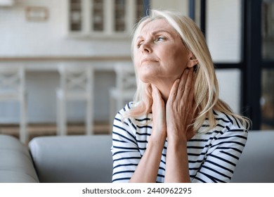 Unhealthy mature woman holding hands on neck, touching lymph nodes. Feeling discomfort, painful sensations, difficult to swallow, throat pain, irritation - Powered by Shutterstock