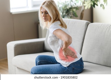 Unhealthy Middle Aged Woman Stand Up From Couch In Living Room Touches Back, Suffer From Back Pain. Sad Mature Female Suffers From Arthritis, Radiculitis, Backache Pain