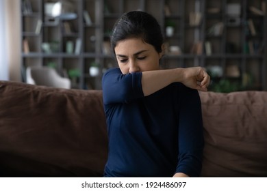 Unhealthy Millennial Indian Woman Cough Sneeze In Elbow Struggle With Covid-19 Coronavirus At Home. Sick Young Ethnic Female Feel Tired Sick Having Flu Or Cold. Corona Virus, Health Problem Concept.