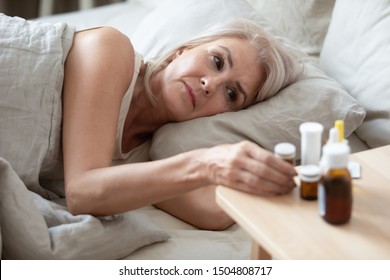 Unhealthy Older Woman Taking Pills From Bedside Table Close Up, Unhappy Mature Female Lying In Bed, Taking Medicine From Cold Or Insomnia, Suffering From Flu Or Seasonal Fever, Treatment Concept