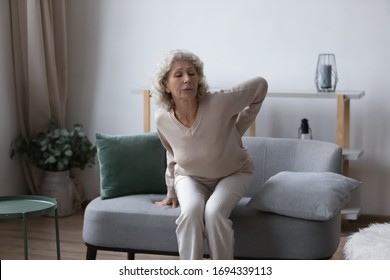 Unhealthy Senior Elderly Woman Getting Up From Sofa, Touching Having Painful Feelings In Back. Unhappy Middle Aged Grandmother Suffering From Chronic Lower Lumbar Pain, Radiculitis Arthritis Concept.