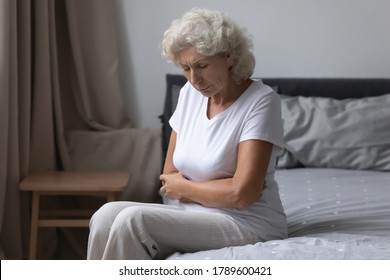 Unhealthy Senior Grey Haired Woman Awakened Woke Up Sit On Bed In Bedroom Alone Touch Abdominal, Suffers From Severe Stomach Ache. Diarrhoea, Gastric Ulcer, Gastritis, Gynecological Problems Concept