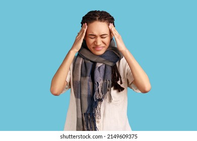 Unhealthy Woman With Black Dreadlocks Wrapped In Scarf, Catching Cold, Rubs Temples To Relieve Headache, Keeps Eyes Shut, Has High Temperature. Indoor Studio Shot Isolated On Blue Background.