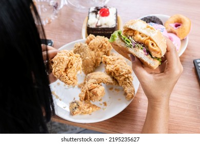 unhealthy woman eating fast food burgers, fried chicken, donuts and desserts, binge eating disorder concept - Shutterstock ID 2195235627