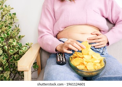 Unhealthy Woman Eating Junk  Potato Chips In Bowl Hand Holding Big, Fat Belly Sitting On Sofa Watching Tv   