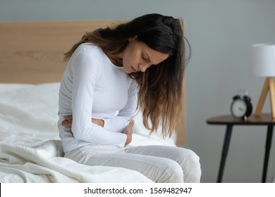 Unhealthy woman sit on bed touch stomach suffer from severe ache abdominal pain indigestion or diarrhoea feels sick, gastric ulcer gastritis problem, menstrual period, unhealthy diet or eating concept