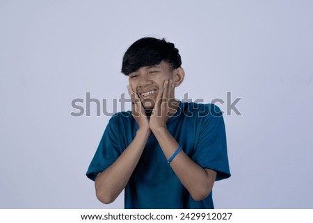 An unhealthy young Asian man suffering from excruciating toothache, isolated in a gray background.