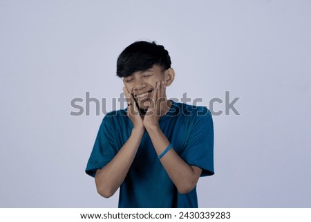 An unhealthy young Asian man suffering from excruciating toothache, isolated in a gray background.