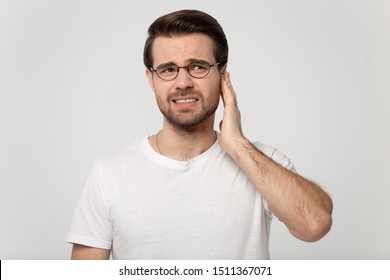 Unhealthy Young Man In Eyeglasses Touching Ear, Suffering From Sudden Throbbing Ear Ache, Looking Aside, Head Shot. Upset Millennial Guy Feeling Unwell, Isolated On Grey White Studio Background.