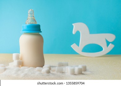 Unhealty Baby Food Concept. The Problem Of Hidden Sugar In Baby Food And Drinks. Bottle With Infant Formula Milk Near Rocker Horse Toy And Sugar.