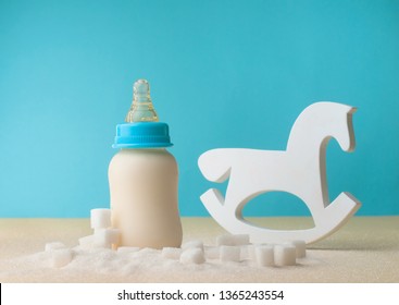 Unhealty Baby Food Concept. The Problem Of Hidden Sugar In Baby Food And Drinks. Bottle With Infant Formula Milk Near Rocker Horse Toy And Sugar.