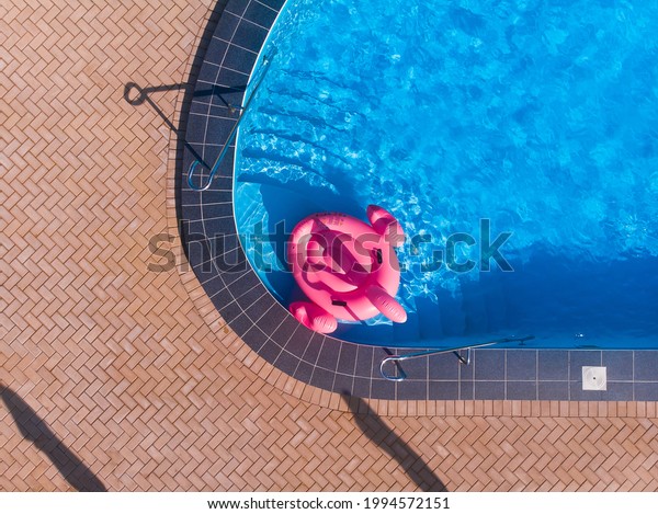 Unicorn\
flamingo float in blue water background, inflatable swim tube. Pool\
party, summer holidays, beach vacation. Fantasy swim flamingo ring\
for summer pool trip. Drone top view from\
above