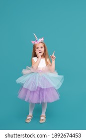Unicorn girl. Funny face. Cute child girl in elegant tulle dress and unicorn headband celebrates birthday  party on colored background. Points to the right