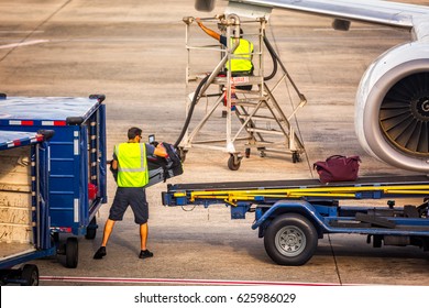 Unidentifiable Airport Worker Loads Pieces Of Baggage Into An Airplane