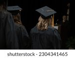 Unidentifiable graduates in black cap, gown, and golden tassel listen to a speech at a community college graduation ceremony.
