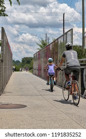 Unidentifiable people biking across a bridge on the Atlanta Beltline on a bright summer day with a blue sky and white clouds