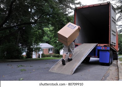 An Unidentifiable Person Is Carrying A Heavy Moving Box Up A Ramp Into The Back Of A Moving Truck (altered Features, Not Recognizable), On A Summer Day In Typical Suburban America