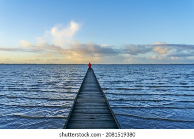 unidentifiable person with red jacket walks on an old footbridge built into the bay Jadebusen in Dangast (Germany)