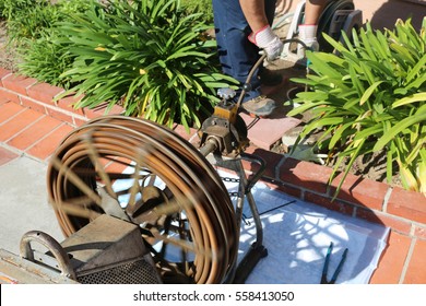 An Unidentifiable plumber unclogs a sewer drain with his Plumbing Snake and tools. 